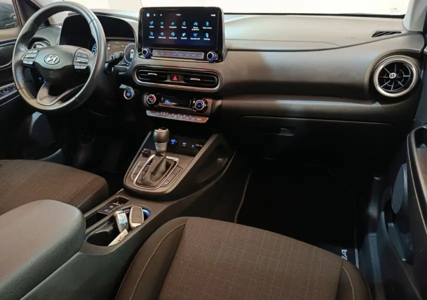 Vue intérieure côté conducteur du Hyundai Kona 1.6 Hybrid 2023, avec tableau de bord noir et écran tactile central.