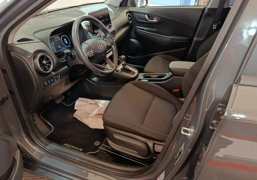 Vue intérieure côté conducteur du Hyundai Kona gris foncé 2023, volant cuir multifonctions et tableau de bord numérique.