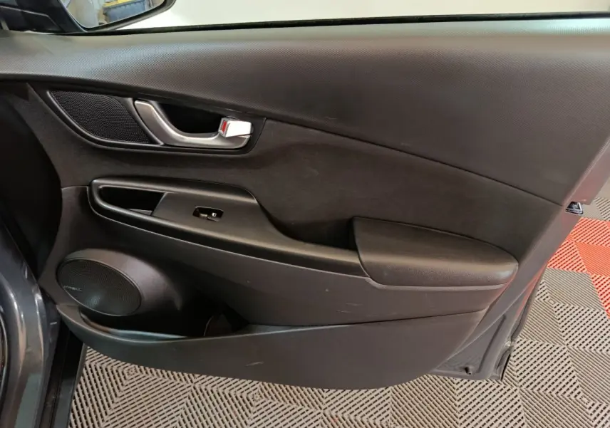 Vue intérieure côté gauche de la porte avant gris foncé du Hyundai Kona 1.6 Hybrid 2023 avec poignée et haut-parleur intégrés.