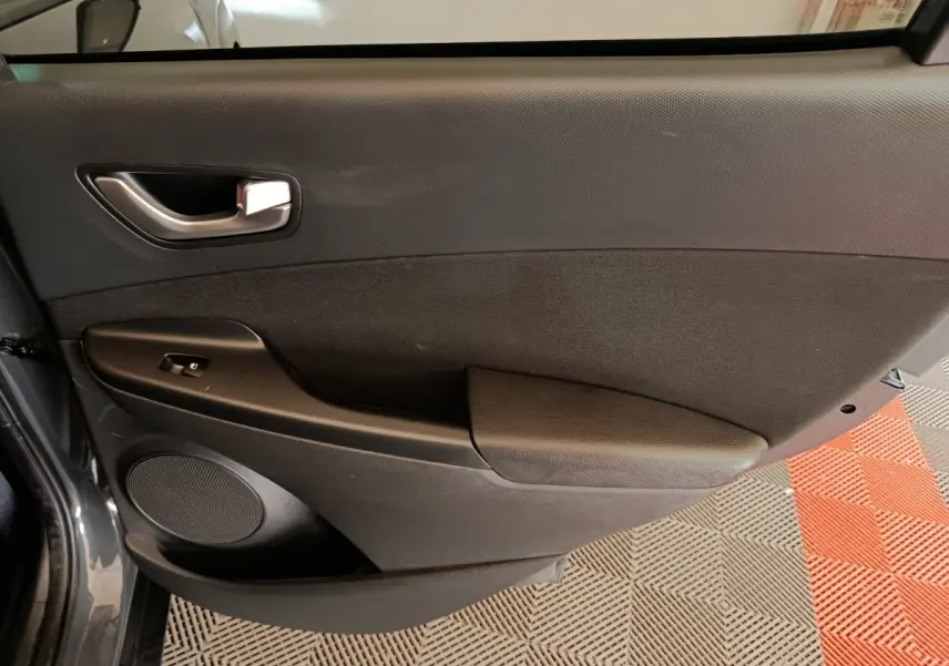 Vue intérieure du panneau de porte avant gauche gris foncé du Hyundai Kona 2023 avec commande de fenêtre électrique.