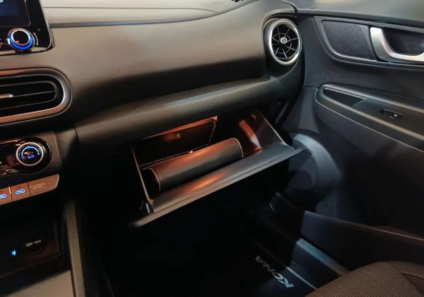 Vue intérieure côté passager du tableau de bord gris foncé du Hyundai Kona 2023 avec boîte à gants ouverte.
