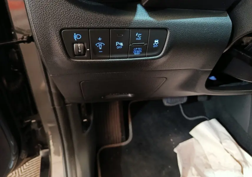 Vue intérieure du tableau de bord côté gauche du Hyundai Kona gris foncé, avec commandes éclairage et assistance au stationnement.