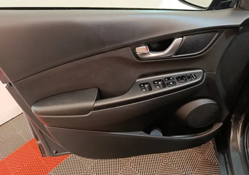 Vue intérieure du panneau de porte côté conducteur d'une Hyundai Kona 1.6 Hybrid 2023, avec commandes électriques et poignée argentée.