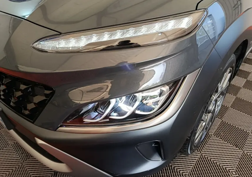 Gros plan sur le phare avant droit et la calandre d’un Hyundai Kona gris foncé 2023 avec feux LED et jante alliage.