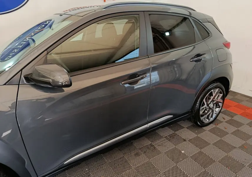 Vue de profil côté gauche d’un Hyundai Kona gris foncé 2023 avec jantes alliage et rétroviseur assorti.