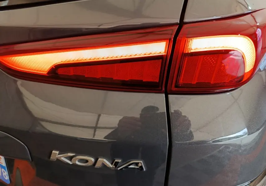 Gros plan sur le feu arrière droit rouge allumé d’un Hyundai Kona gris foncé avec logo visible sur la carrosserie.
