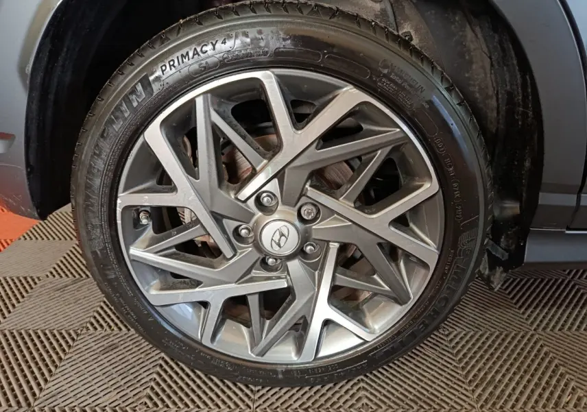 Gros plan sur la jante alliage grise au design géométrique du Hyundai Kona gris foncé, roue avant droite visible.