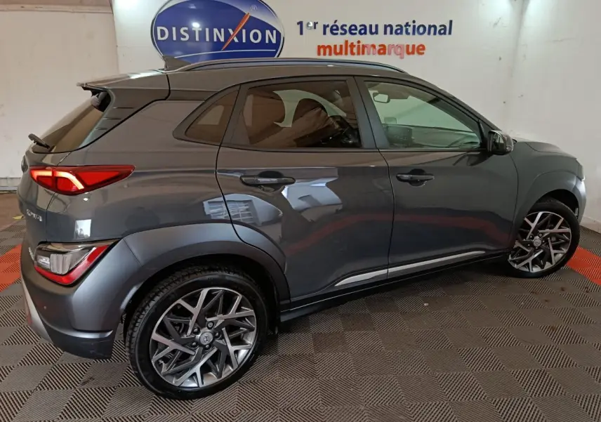 Vue côté droit d’un Hyundai Kona 1.6 Hybrid gris foncé, avec jantes alliage et feux arrière LED visibles en intérieur showroom.