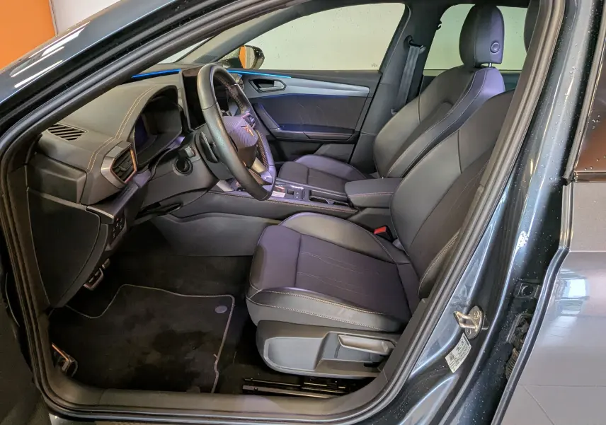 Vue intérieure côté conducteur de la CUPRA LEON ST gris magnetic, montrant sièges sport en cuir et volant multifonction.