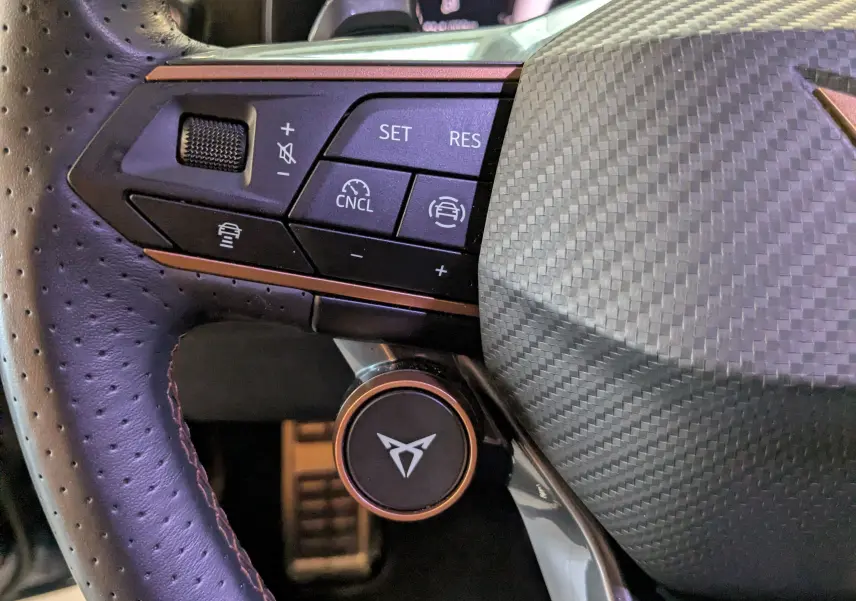 Gros plan sur le volant cuir perforé du CUPRA LEON ST 2025 avec commandes multifonctions et insert carbone.