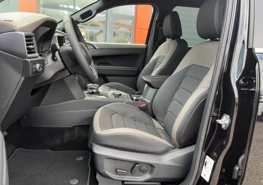 Vue intérieure côté conducteur du Volkswagen Amarok noir 2025, mettant en valeur les sièges cuir bi-ton et le volant multifonctions.