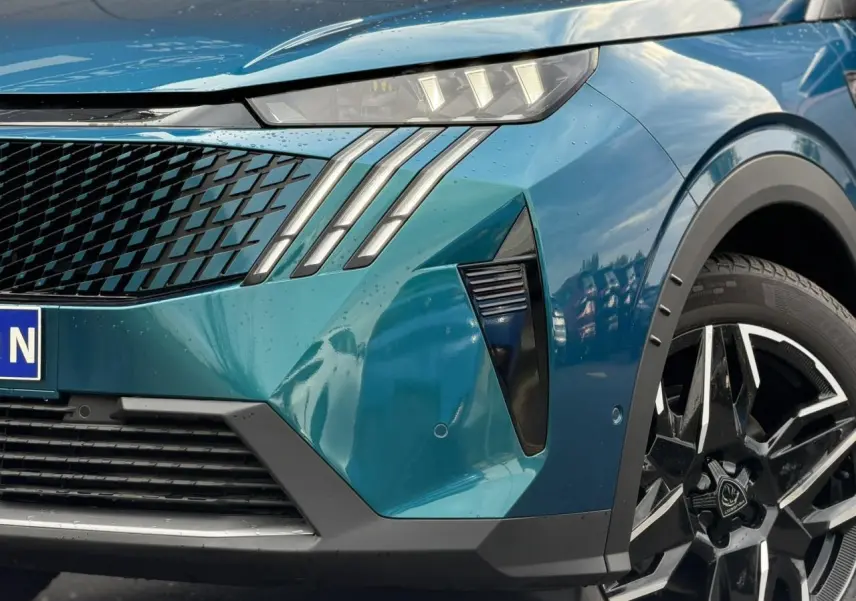 Gros plan sur l'avant droit bleu Obsession du Peugeot 3008 Hybrid 145 GT avec phares à griffes LED et jante alliage noire.