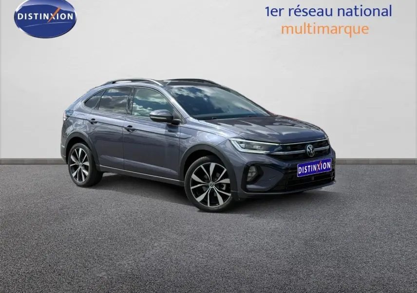 Volkswagen Taigo gris Ascot en 3/4 avant droit, avec jantes alu et barres de toit visibles.