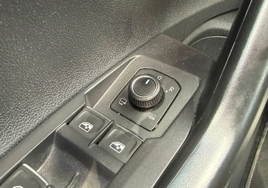 Gros plan sur les commandes de réglage des rétroviseurs et des vitres côté conducteur d’un Volkswagen Taigo gris.
