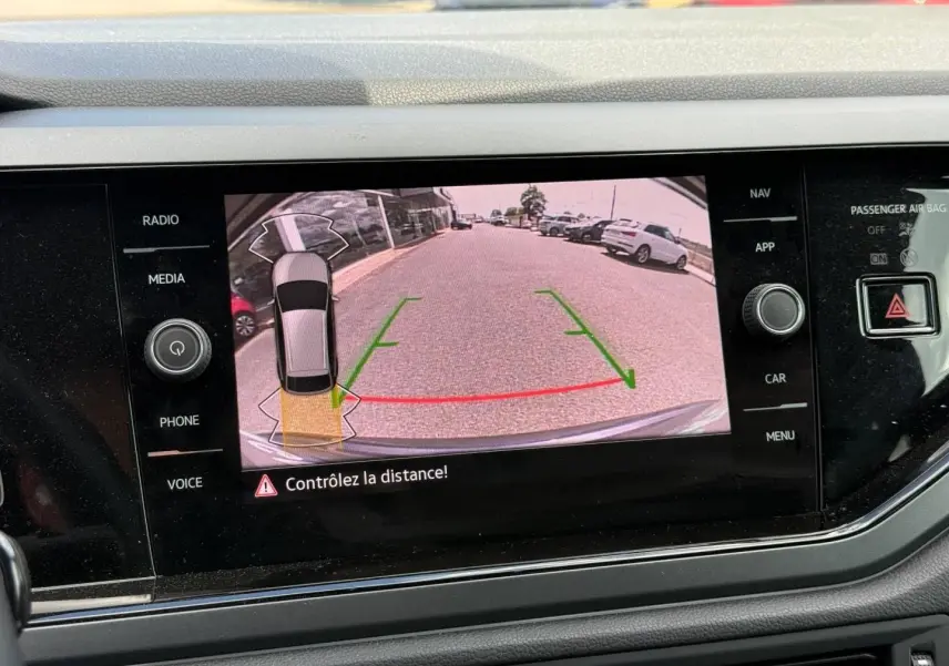 Vue de l'écran tactile montrant la caméra de recul active du Volkswagen Taigo gris, avec lignes de guidage vertes et rouges.