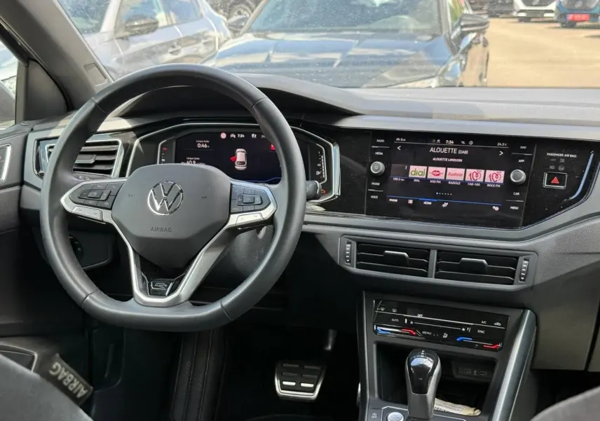 Vue intérieure du poste de conduite du Volkswagen Taigo gris, avec volant cuir multifonction et écran tactile central allumé.