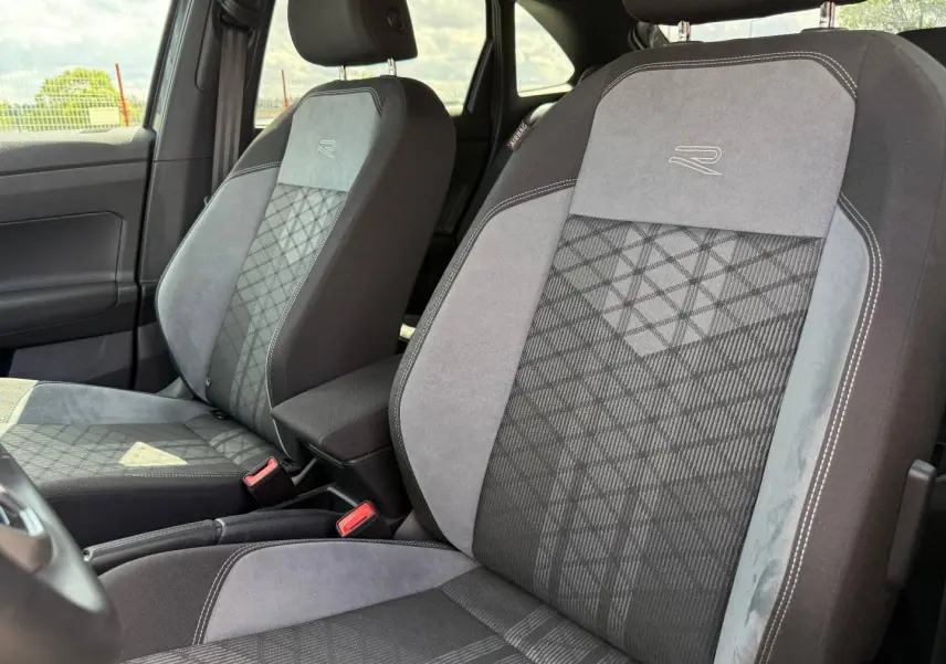 Gros plan sur les sièges avant gris R-Line avec surpiqûres et logo "R" du Volkswagen Taigo 2025.