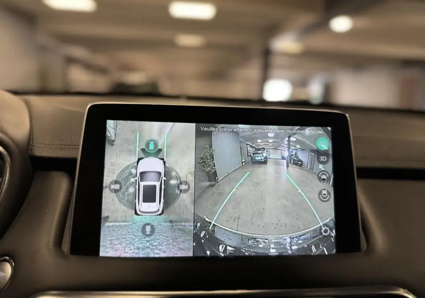 Écran tactile intérieur montrant la caméra 360° et vue arrière du MG MOTOR EHS noir en stationnement dans un garage.