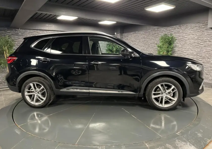 Vue latérale droite du SUV MG EHS noir métallisé avec jantes alliage et contours de vitres chromés en intérieur showroom.