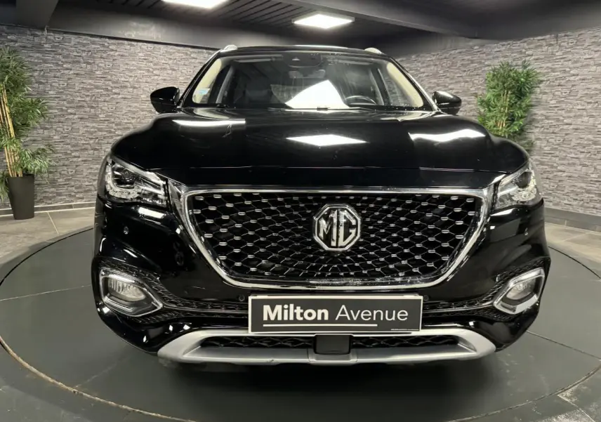 Vue frontale du MG Motor EHS noir métallisé avec calandre hexagonale et logo MG bien visible dans un showroom.