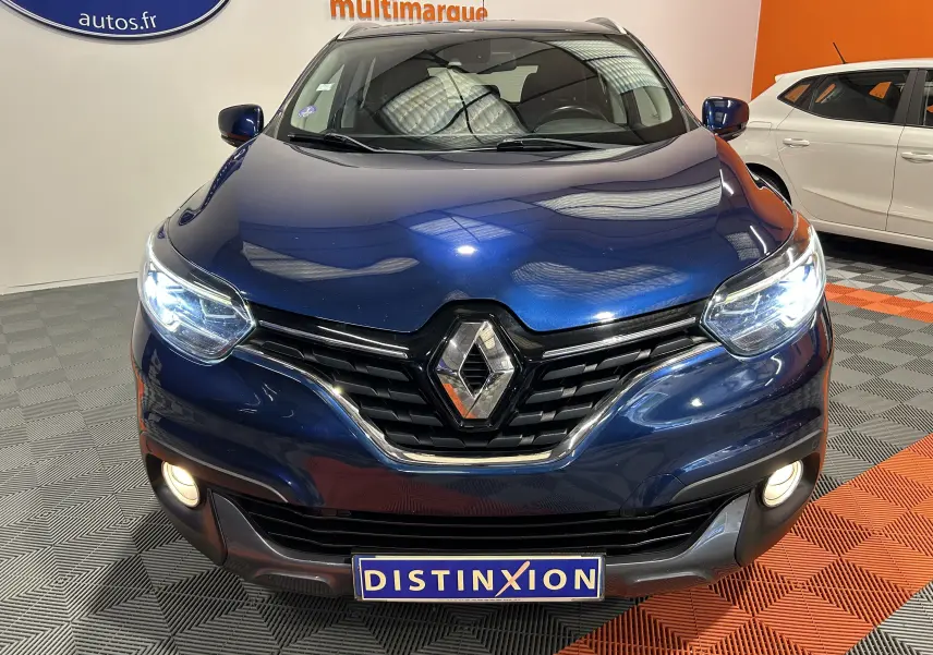 Vue avant rapprochée d'un Renault Kadjar bleu 2017 avec phares allumés et calandre chromée visible en intérieur showroom.