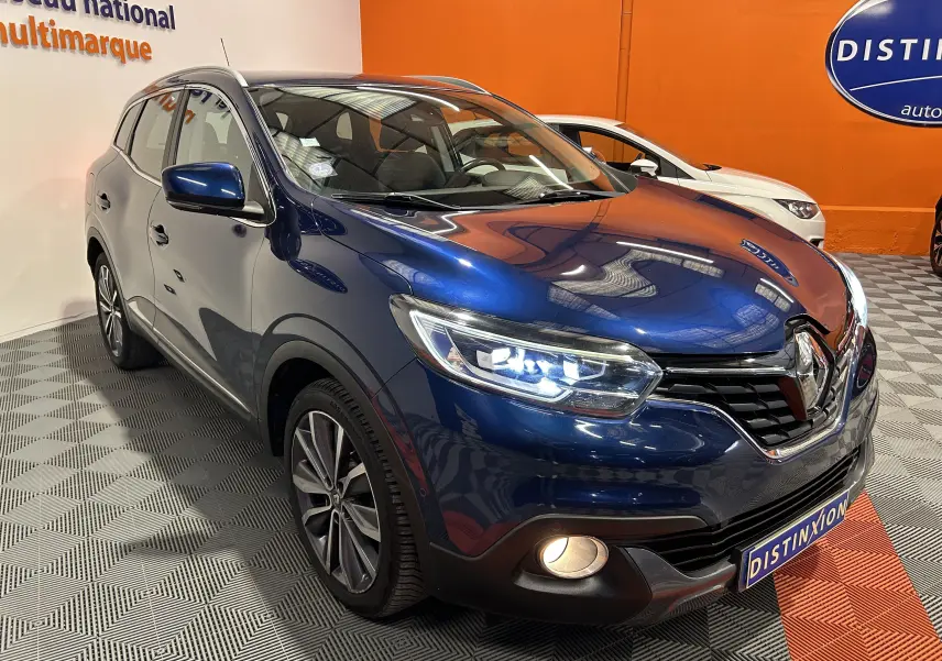 Renault Kadjar bleu en 3/4 avant droit avec phares LED allumés dans un showroom orange.