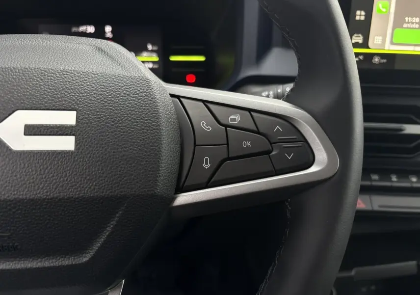 Gros plan sur les commandes au volant côté droit du Dacia Duster blanc glacier, avec écran tactile en arrière-plan.