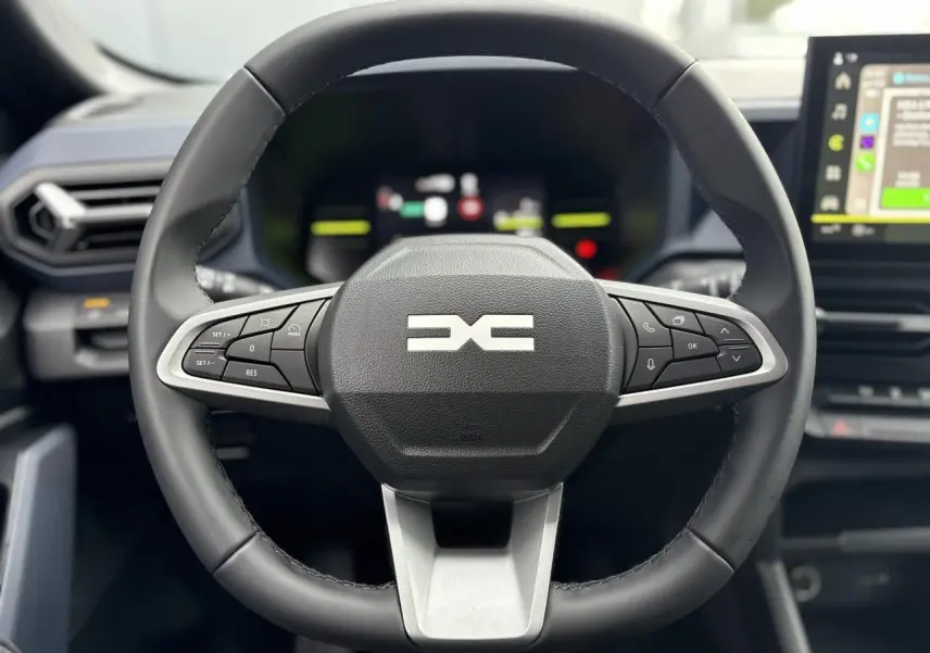 Volant noir de DACIA Duster 2025 en vue frontale, avec commandes intégrées et écran tactile en arrière-plan.