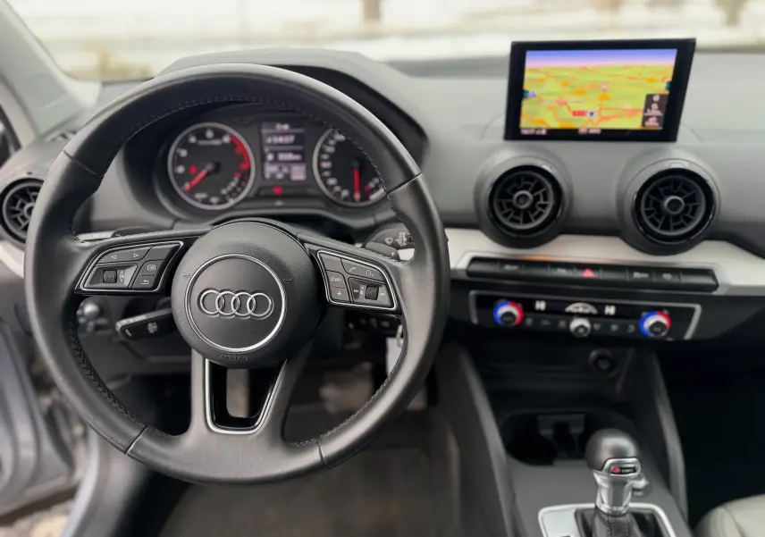 Vue intérieure centrée sur le volant noir d’un Audi Q2 2017 avec tableau de bord et écran GPS en arrière-plan.