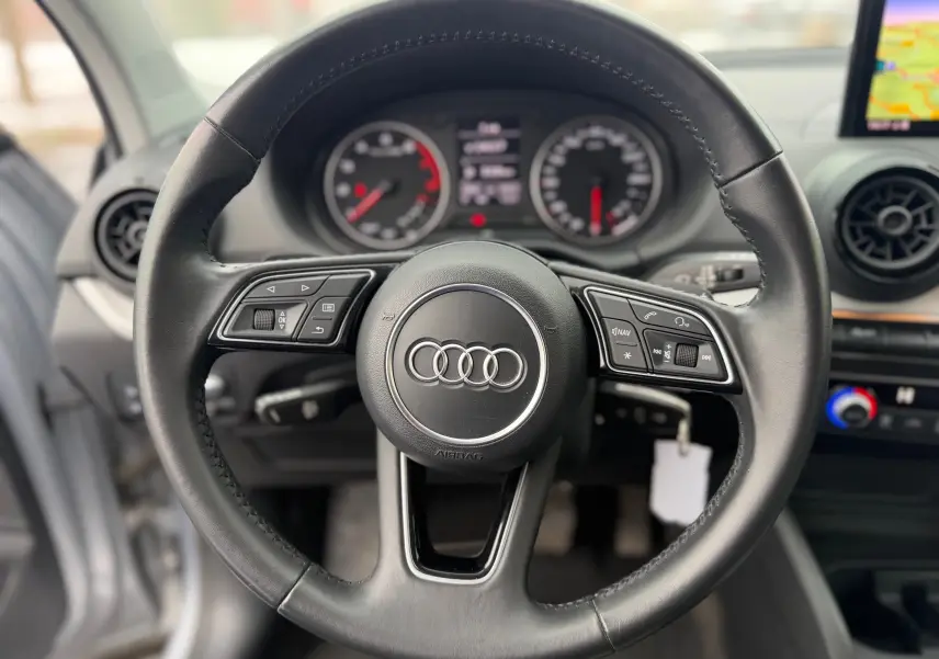 Vue rapprochée du volant en cuir noir de l'Audi Q2 2017 avec commandes multifonctions et tableau de bord en arrière-plan.