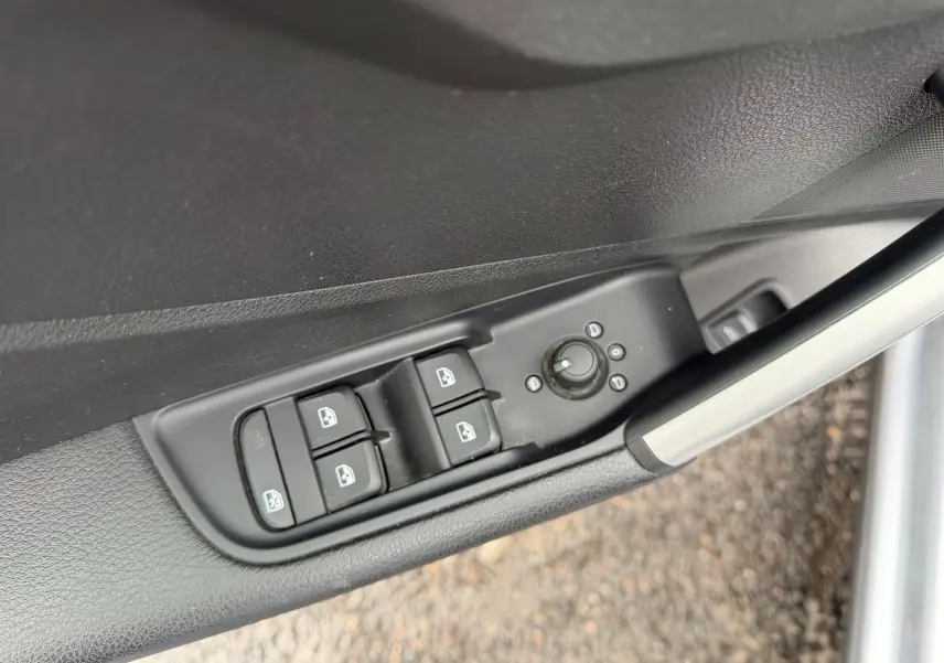 Gros plan sur les commandes de lève-vitres et réglage des rétroviseurs sur la porte côté gauche d’un Audi Q2 gris aluminium.