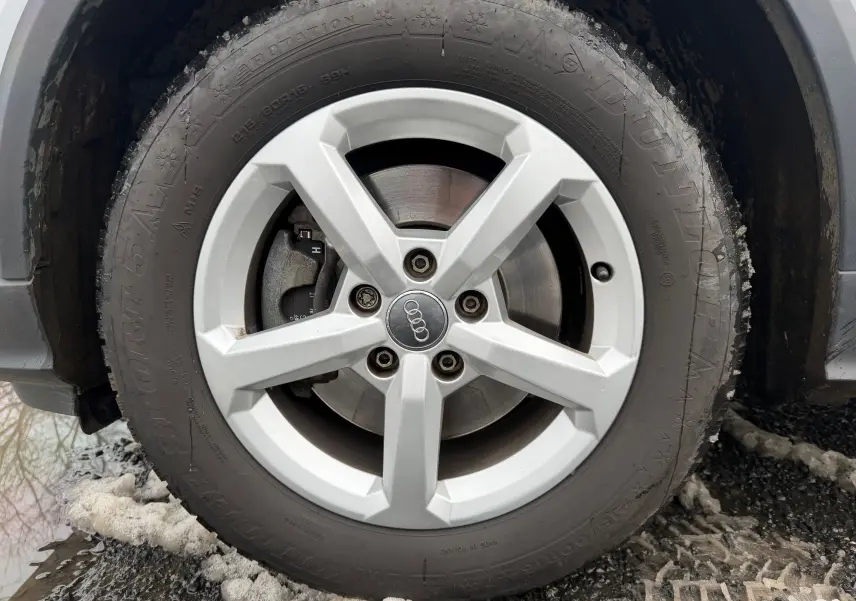 Gros plan sur la roue avant droite d'un Audi Q2 gris aluminium, avec jante alliage 5 branches et pneu hiver Dunlop.