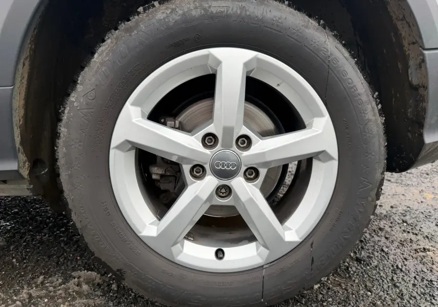 Gros plan sur la roue avant droite d’un Audi Q2 gris aluminium, avec jante alliage 5 branches et logo Audi central.