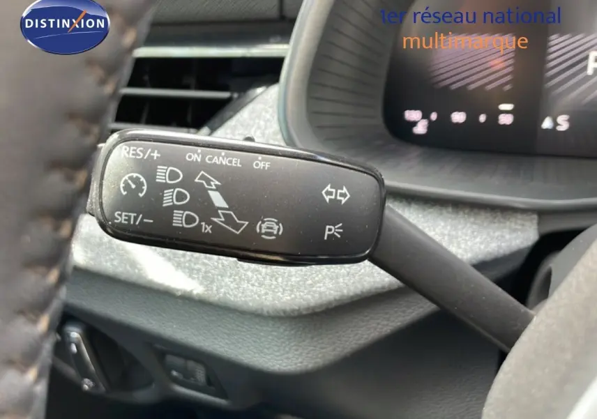 Gros plan sur la commande de régulateur de vitesse à gauche du volant dans l’habitacle d’une Skoda Scala blanc glacier.