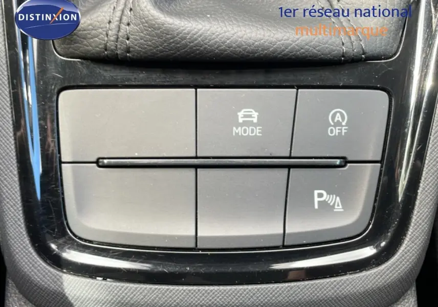 Gros plan sur les boutons de commande du mode de conduite et de l'aide au stationnement dans une Skoda Scala blanc glacier 2025.