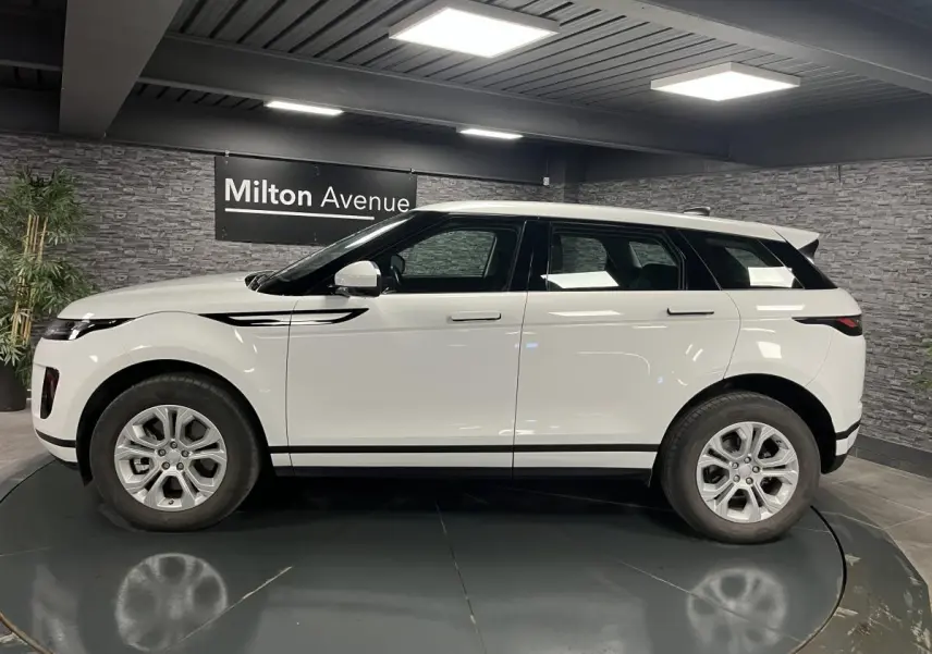 Range Rover Evoque blanc vu de profil côté gauche dans un showroom avec murs en pierre grise.