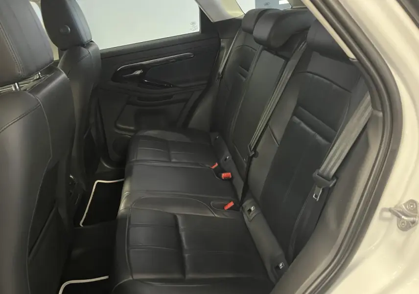 Vue côté droit de l'habitacle arrière du Range Rover Evoque blanc, sièges cuir noir et ceintures visibles.