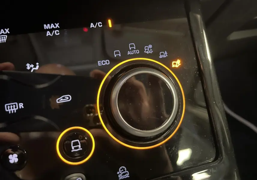 Gros plan sur la commande de modes de conduite du Range Rover Evoque blanc, avec éclairage orange autour du bouton central.