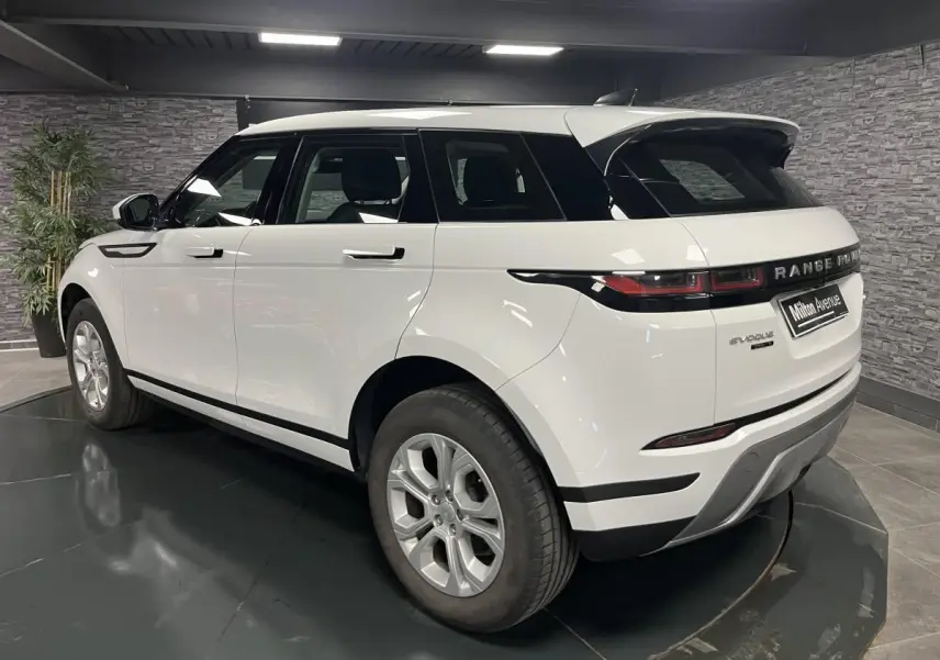 Vue 3/4 arrière droite d'un Range Rover Evoque blanc avec jantes 18 pouces et toit assorti en intérieur showroom.