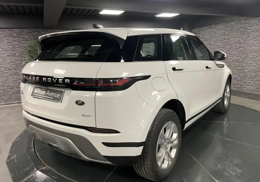 Vue 3/4 arrière droit d'un Range Rover Evoque blanc avec toit noir et jantes argentées en showroom.