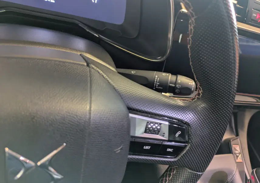 Gros plan sur le volant perforé noir du DS7 2019 rouge, avec commandes intégrées et compteur partiellement visible.