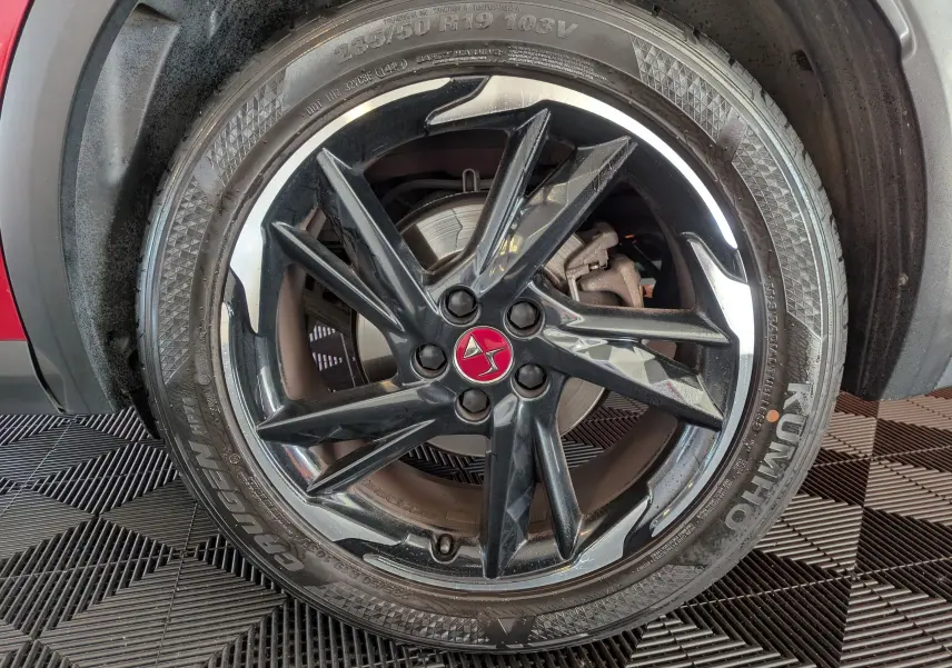 Gros plan sur la roue avant gauche du DS7 rouge 2019, jante noire brillante avec logo DS rouge au centre.