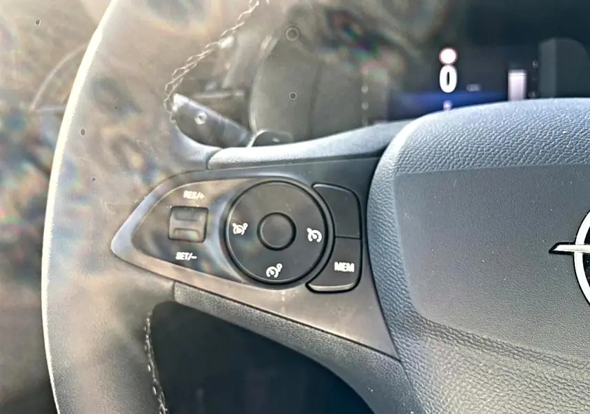 Gros plan sur la partie gauche du volant sport noir de l’Opel Corsa 2025 avec commandes multifonctions et logo Opel visible.