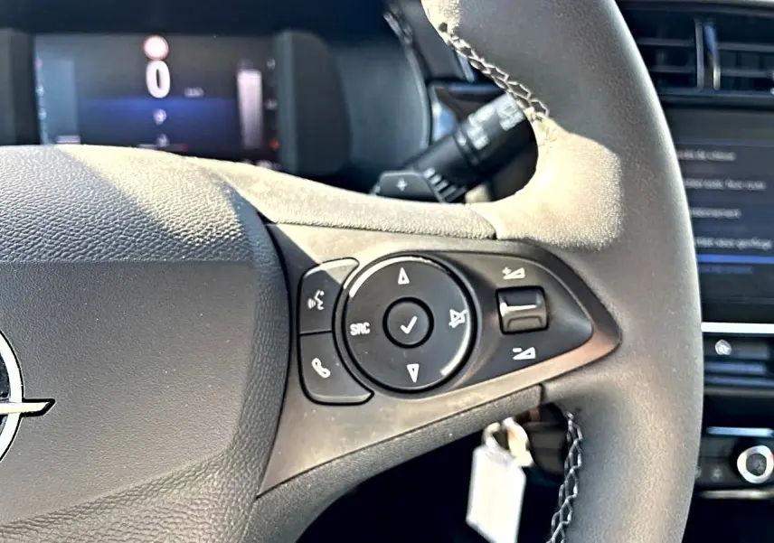 Gros plan sur le volant multifonction noir de l’Opel Corsa 1.2 turbo 100 edition, avec commandes audio visibles.