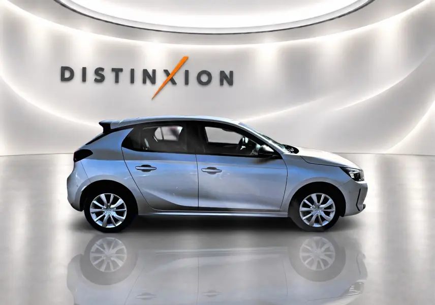 Profil droit d'une Opel Corsa gris alu 2025 dans un showroom lumineux avec reflet au sol et logo Distinxion en arrière-plan.