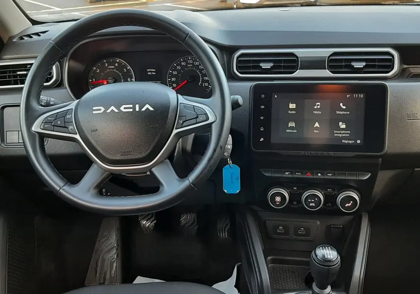 Vue intérieure centrée sur le volant et la console centrale du Dacia Duster 2023, avec boîte manuelle et écran tactile.