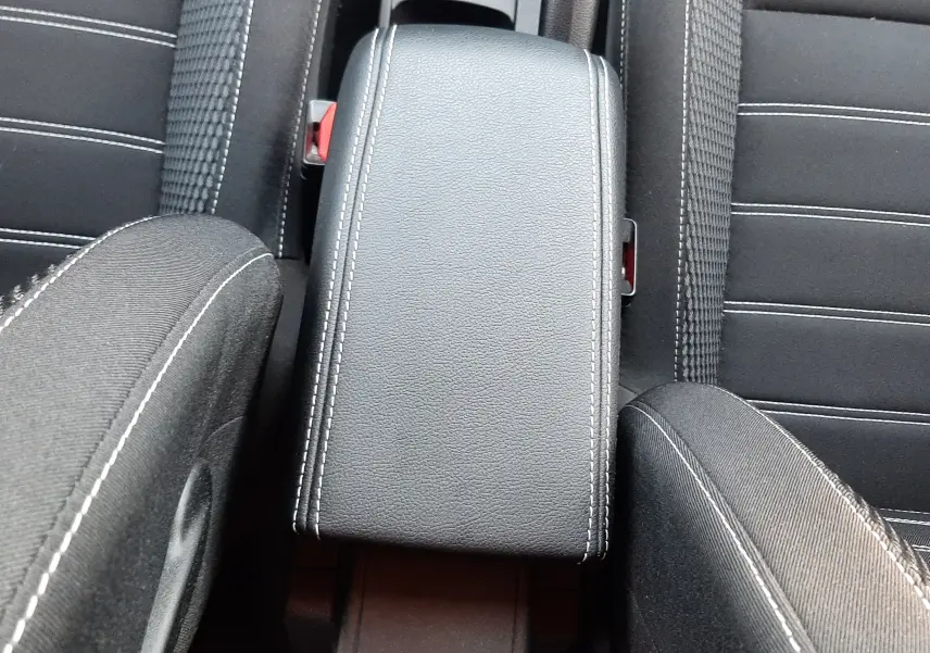 Vue plongeante sur l'accoudoir central noir avec surpiqûres blanches entre les sièges avant du Dacia Duster 2023.