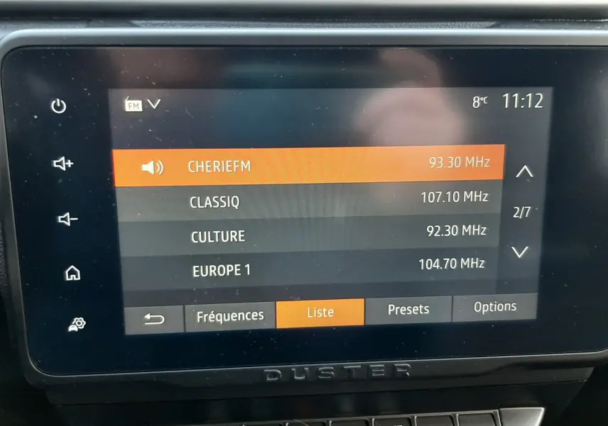 Écran tactile central du tableau de bord du Dacia Duster 2023 affichant les stations radio FM, avec commandes climatisation en dessous.
