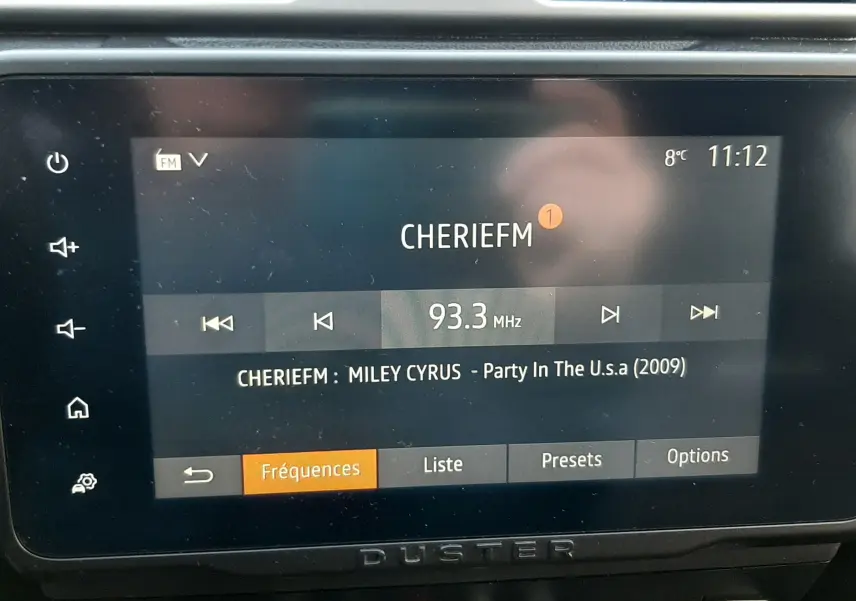 Écran tactile central du Dacia Duster 2023 affichant la radio FM avec la station CHERIEFM et la chanson en cours.