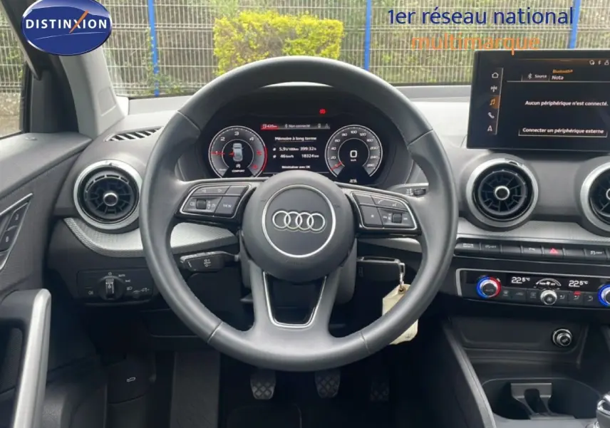 Vue intérieure centrée sur le volant noir de l'Audi Q2 30 TDI S-Line avec tableau de bord numérique et commandes au volant.